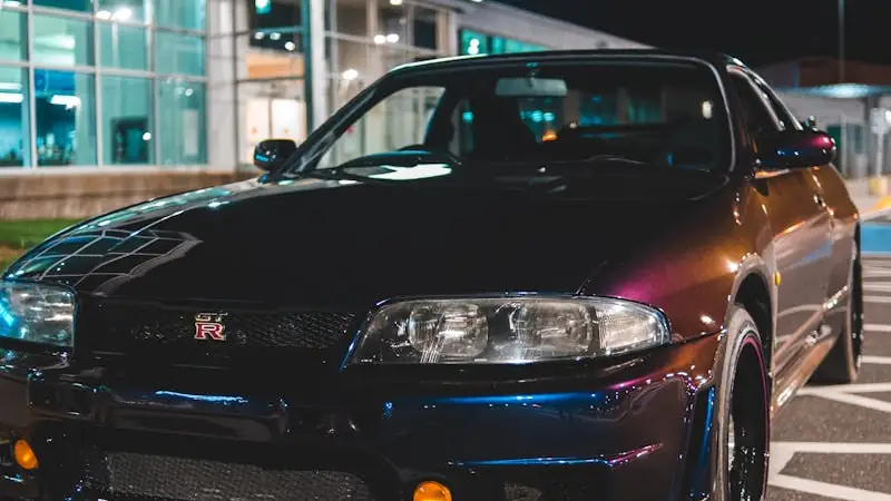 Dunkles Sportcoupé bei Nacht vor einem beleuchteten Gebäude